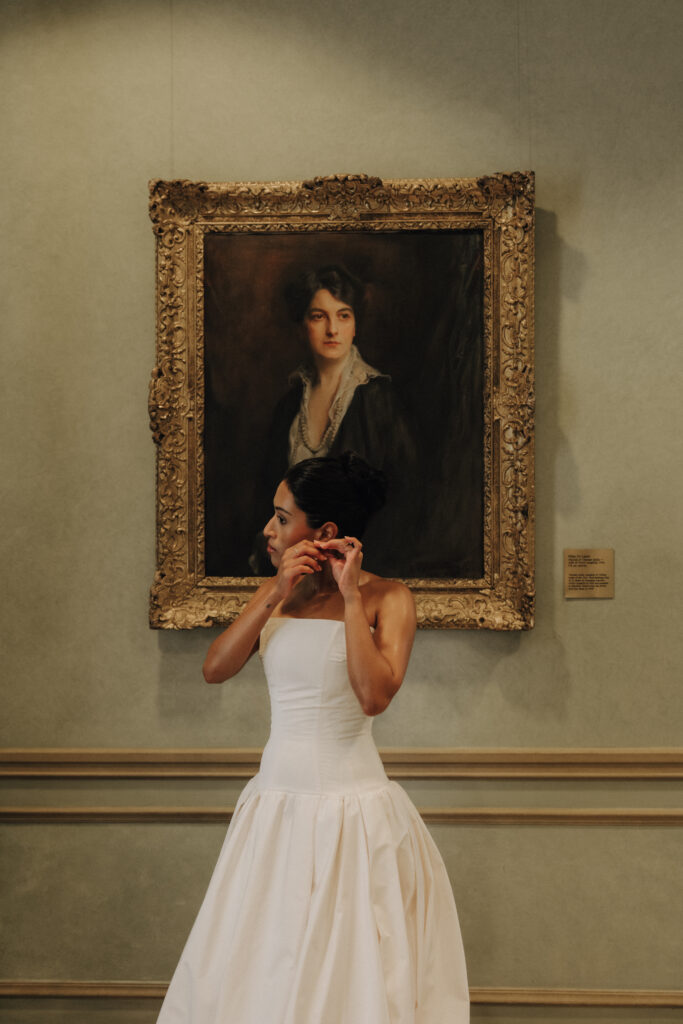 bride standing in front of a framed portrait putting on an earring