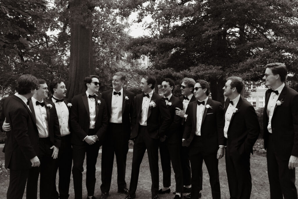 groom and groomsmen in black tuxes laughing together outside of meridian house venue, photographed by dc wedding photographer ashton sotiro